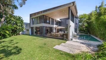 A modern two-story house with a large glass facade, a swimming pool, and a well-maintained lawn.