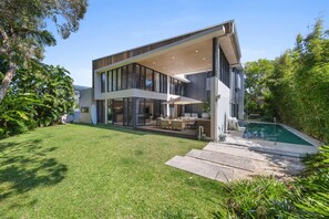 A modern two-story house with a large glass facade, a swimming pool, and a well-maintained lawn.