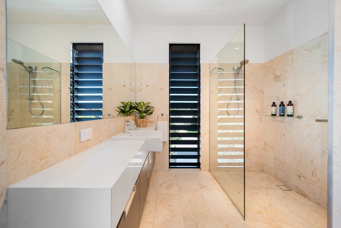 A modern bathroom with a large mirror, two sinks, a shower, and a glass-enclosed shower area.