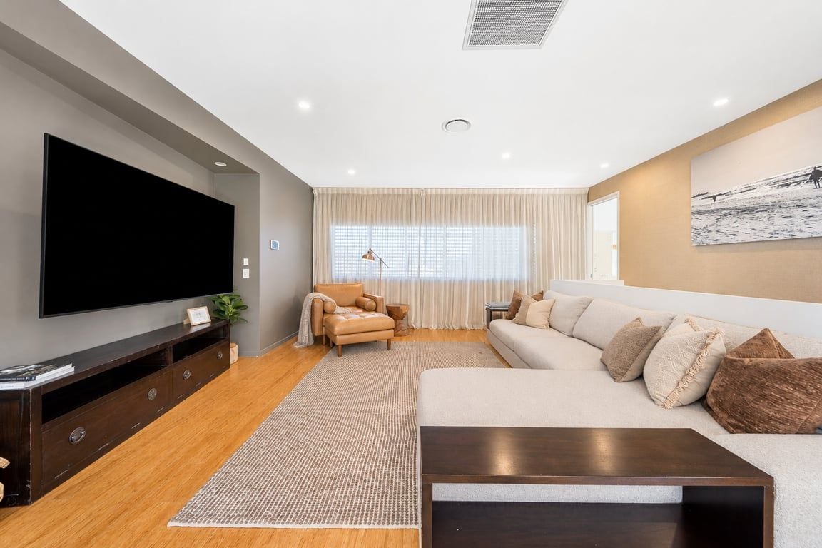 A modern living room with a flat-screen TV, a sofa, a coffee table, and a large window with curtains.