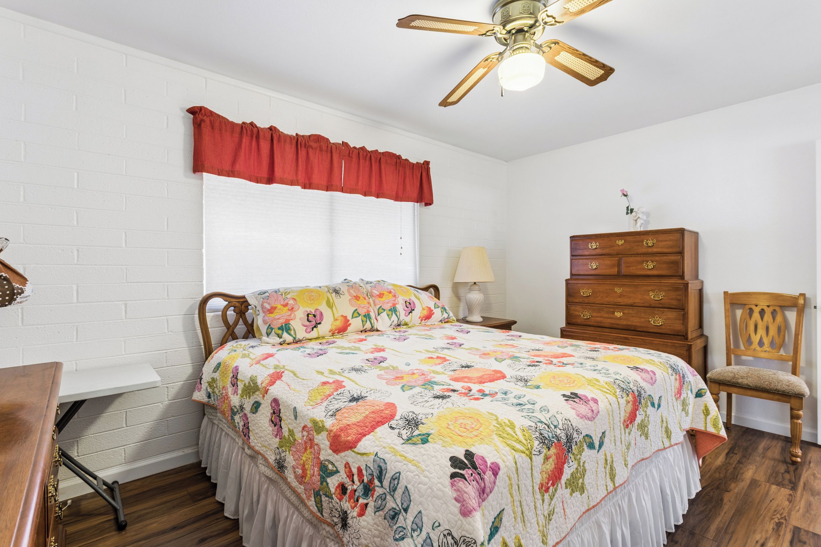 Un dormitorio con cama, cómoda, silla y ventilador de techo.