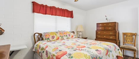 Un dormitorio con cama, cómoda, silla y ventilador de techo.