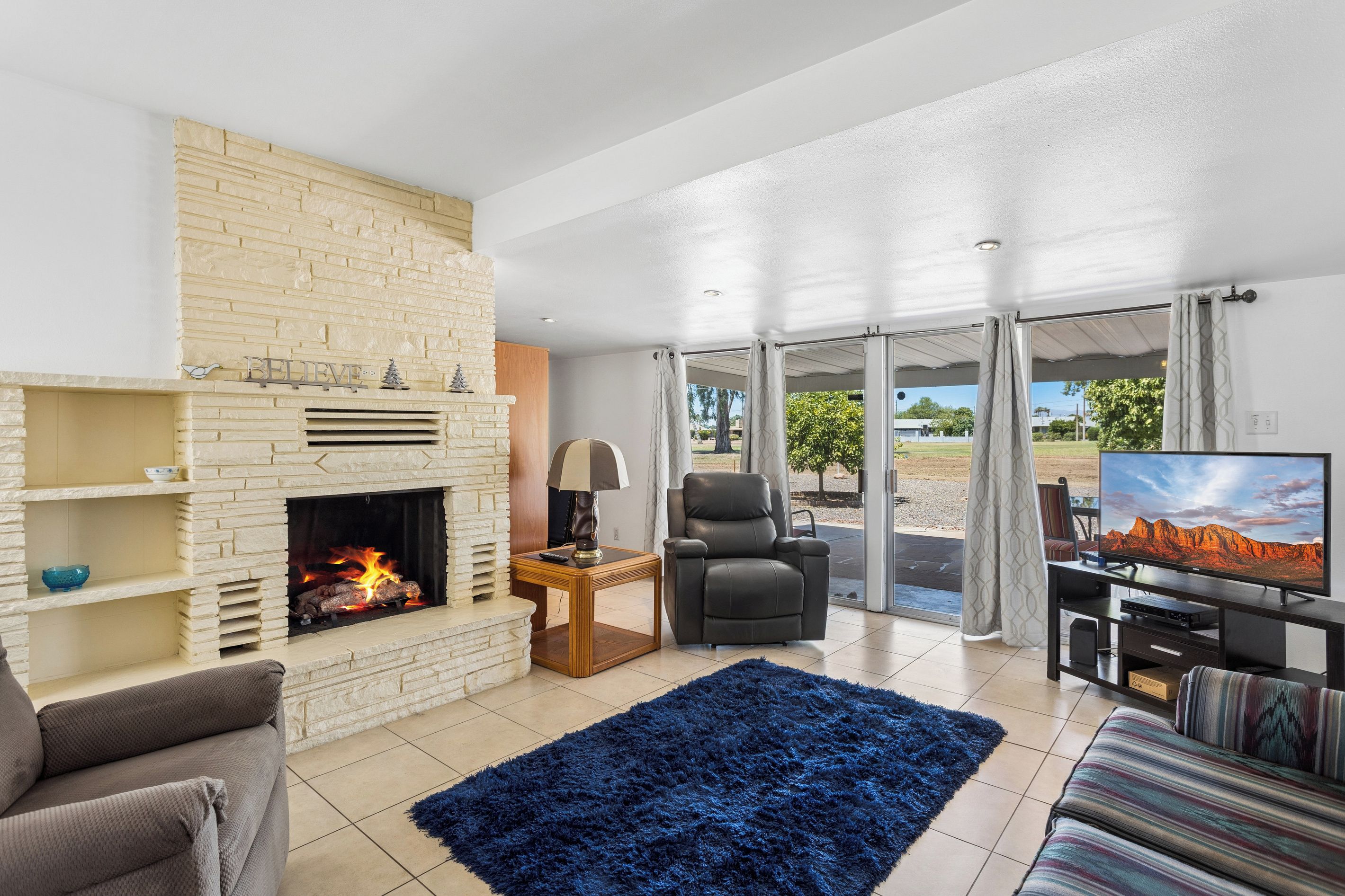 A living room with a fireplace, a sofa, a TV, and a view of the outdoors.