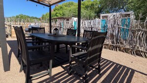 An outdoor covered patio with a table and chairs, surrounded by a gravel floor and a metal fence. - The Palisade Tent at Gateway Glamping (Gateway)