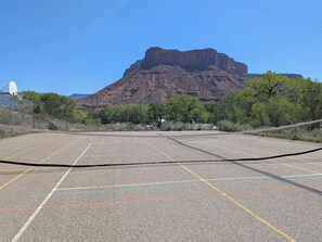 An outdoor basketball court with a net, surrounded by a fence, and a mountain in the background.
