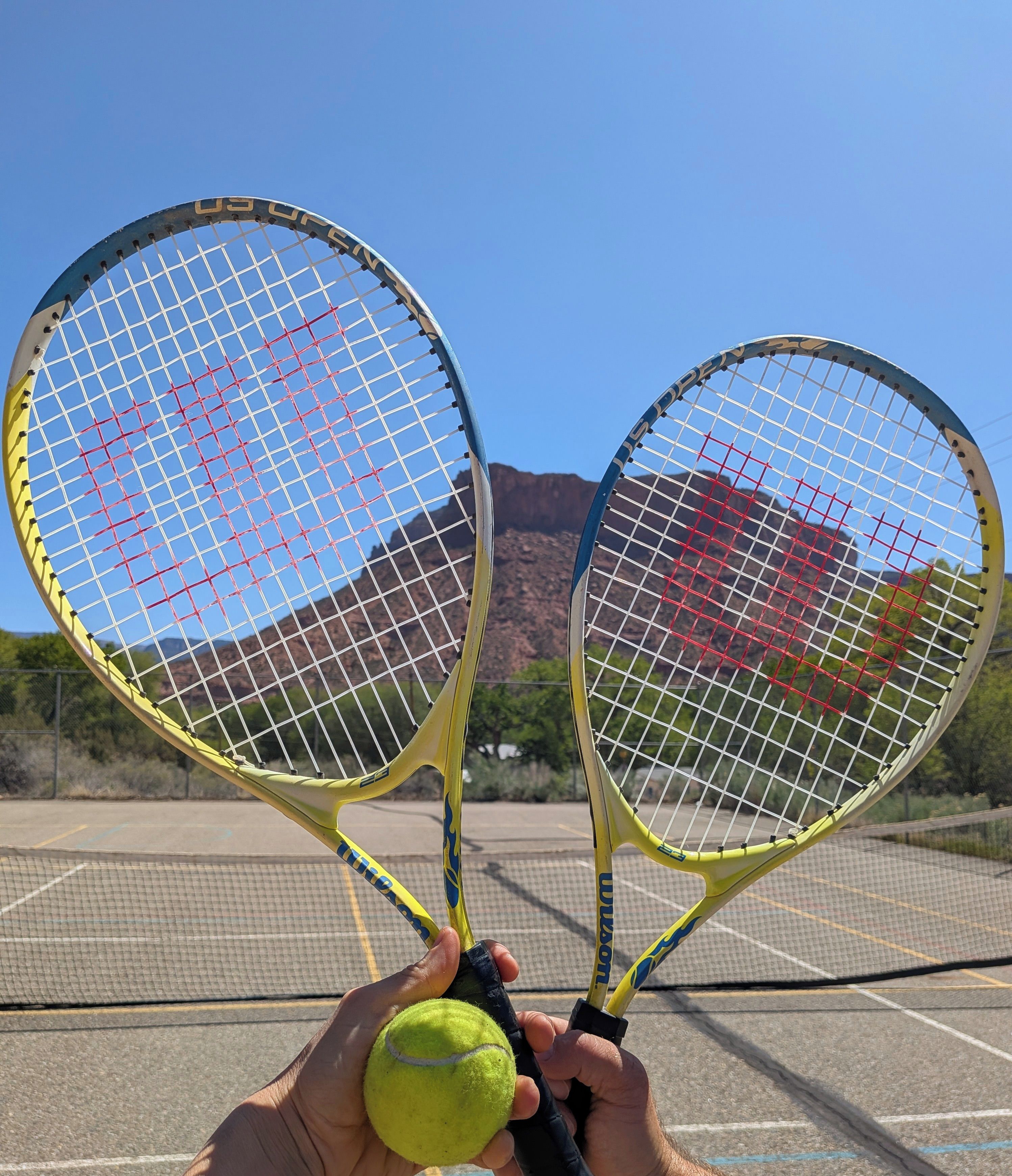 Deux raquettes de tennis et une balle de tennis, tenus par une personne.