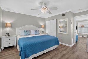 Ein Schlafzimmer mit einem Bett, Nachttischen, einem Deckenventilator, einer Tür und einem Spiegel.