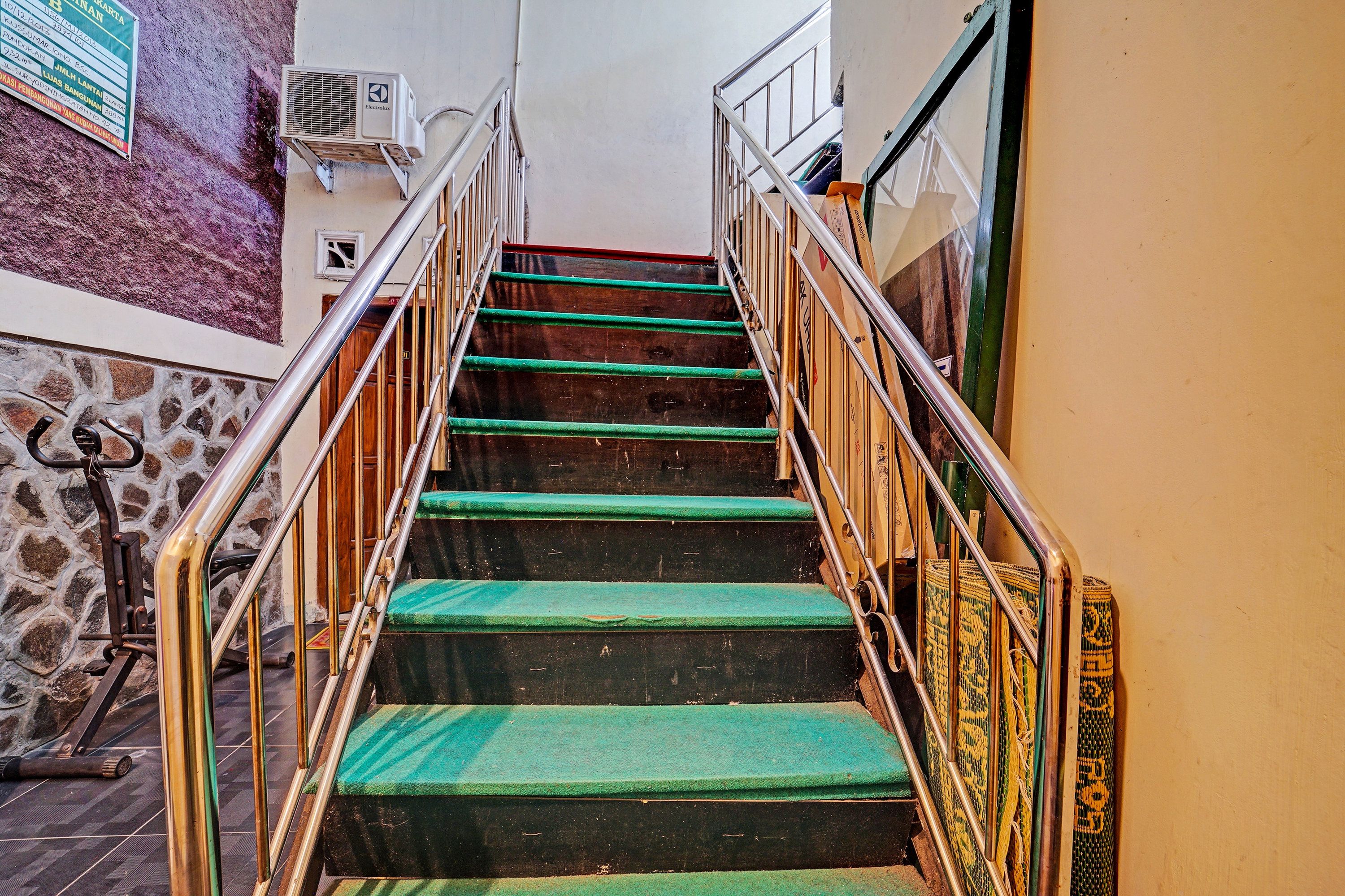 Una escalera con peldaños alfombrados de verde y barandillas de metal, que conduce a un piso superior.