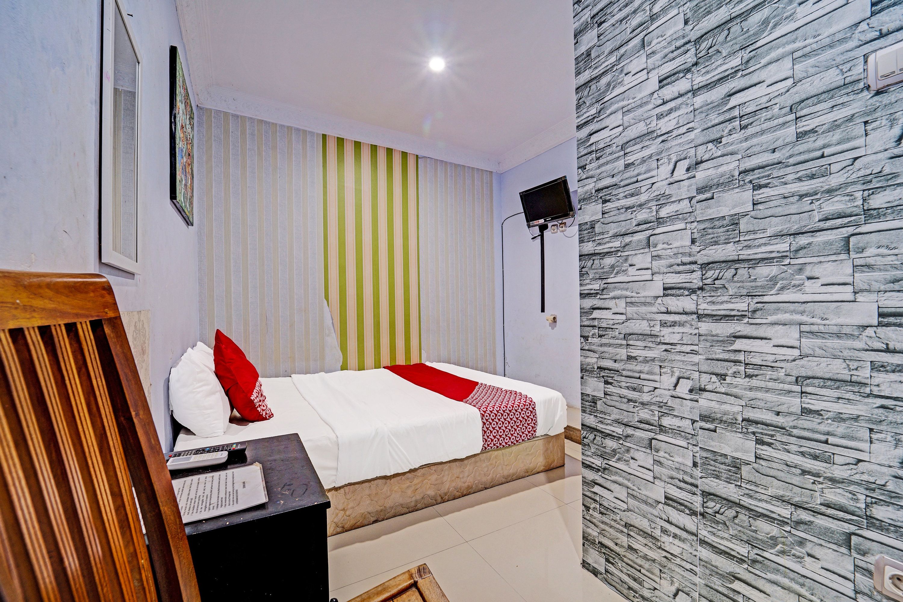 Una habitación de hotel con cama, televisión, ventana con cortinas y pared de textura de piedra.
