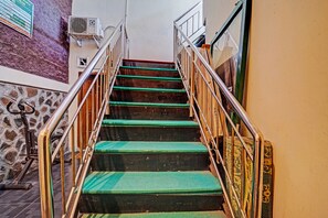 Una escalera con peldaños alfombrados en color verde, barandales de metal y un equipo de aire acondicionado instalado en la pared.