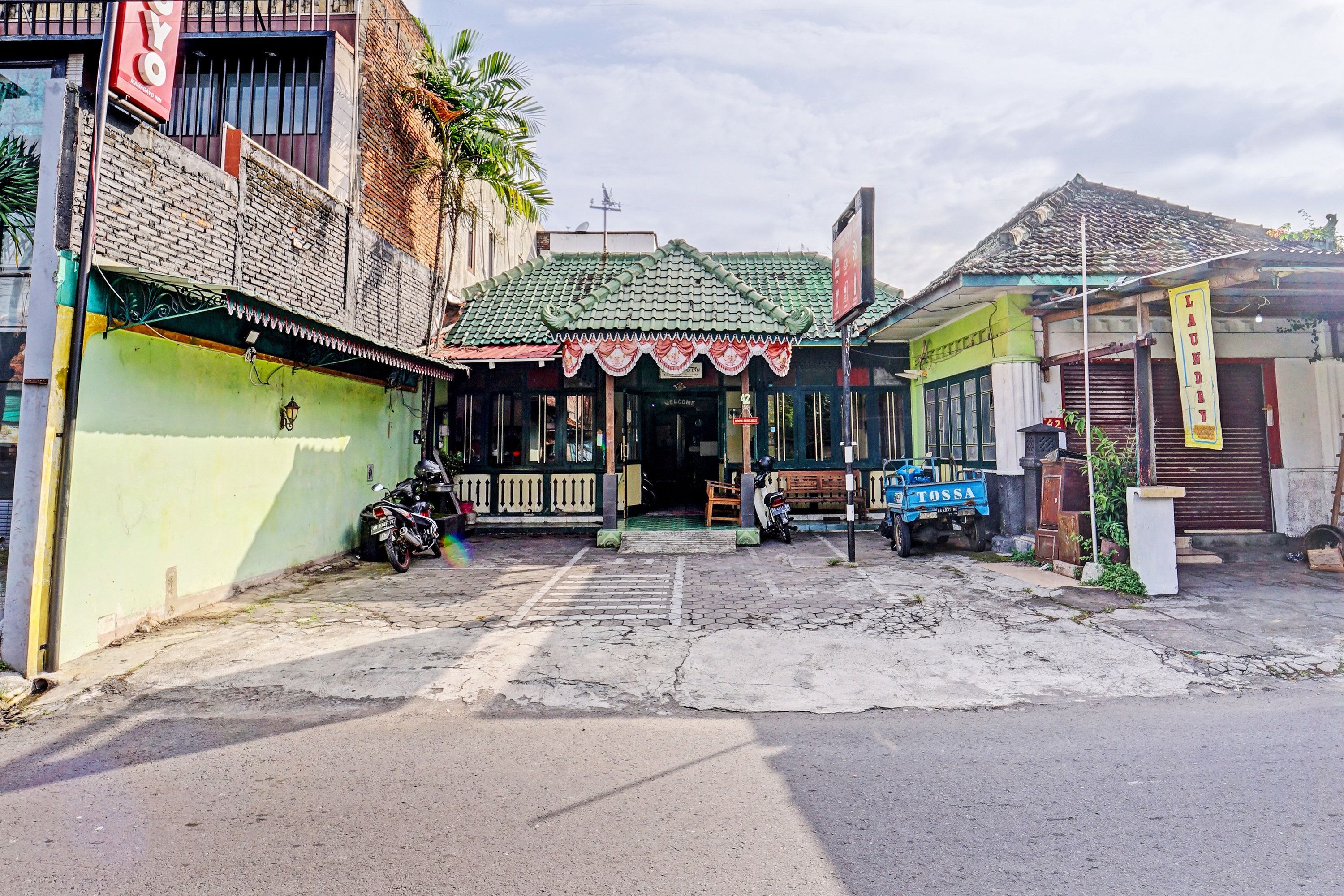 A street view with a building featuring a green roof and a signboard.