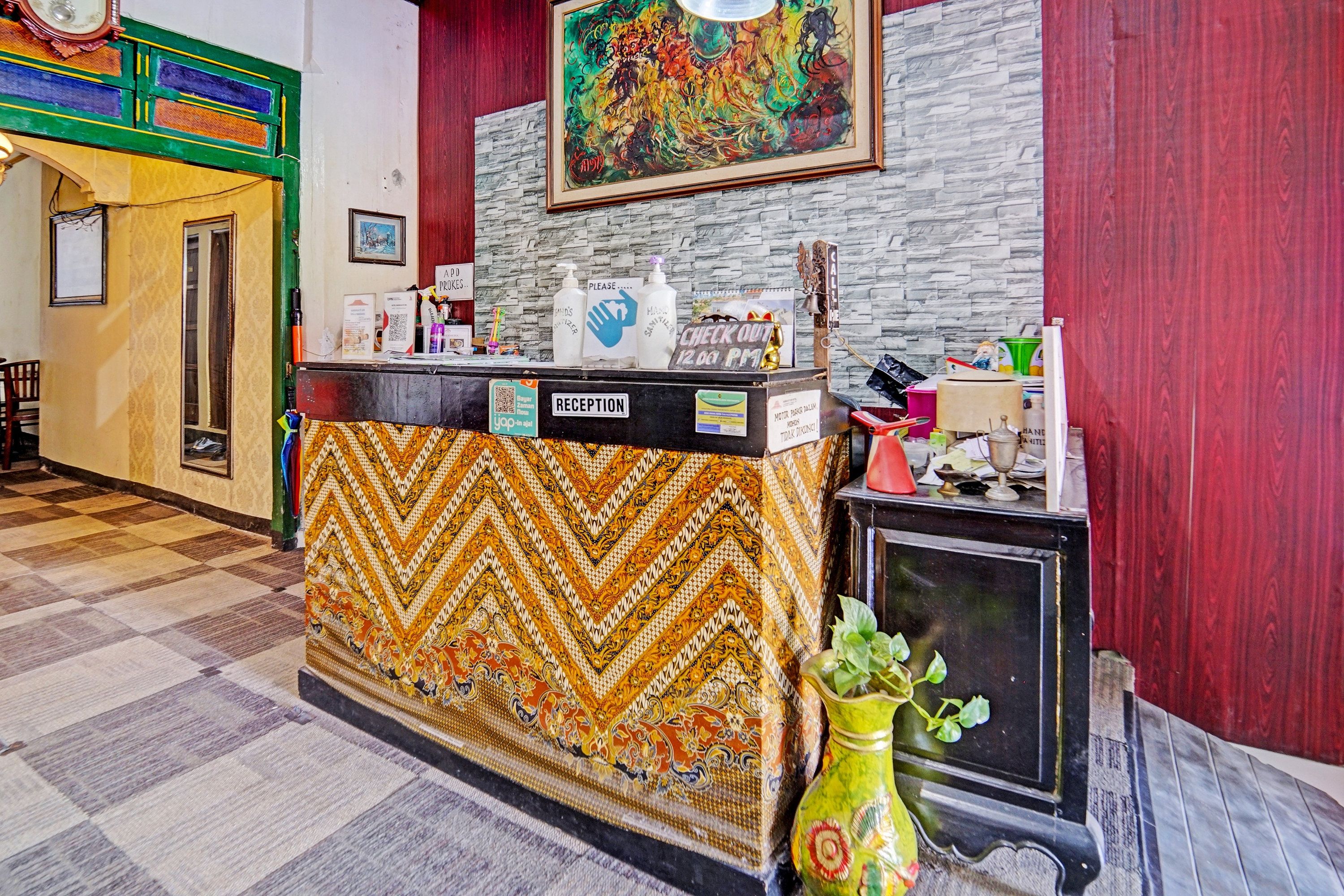 Un área de recepción con alfombra estampada, un mostrador de recepción, un cuadro y un jarrón decorativo.