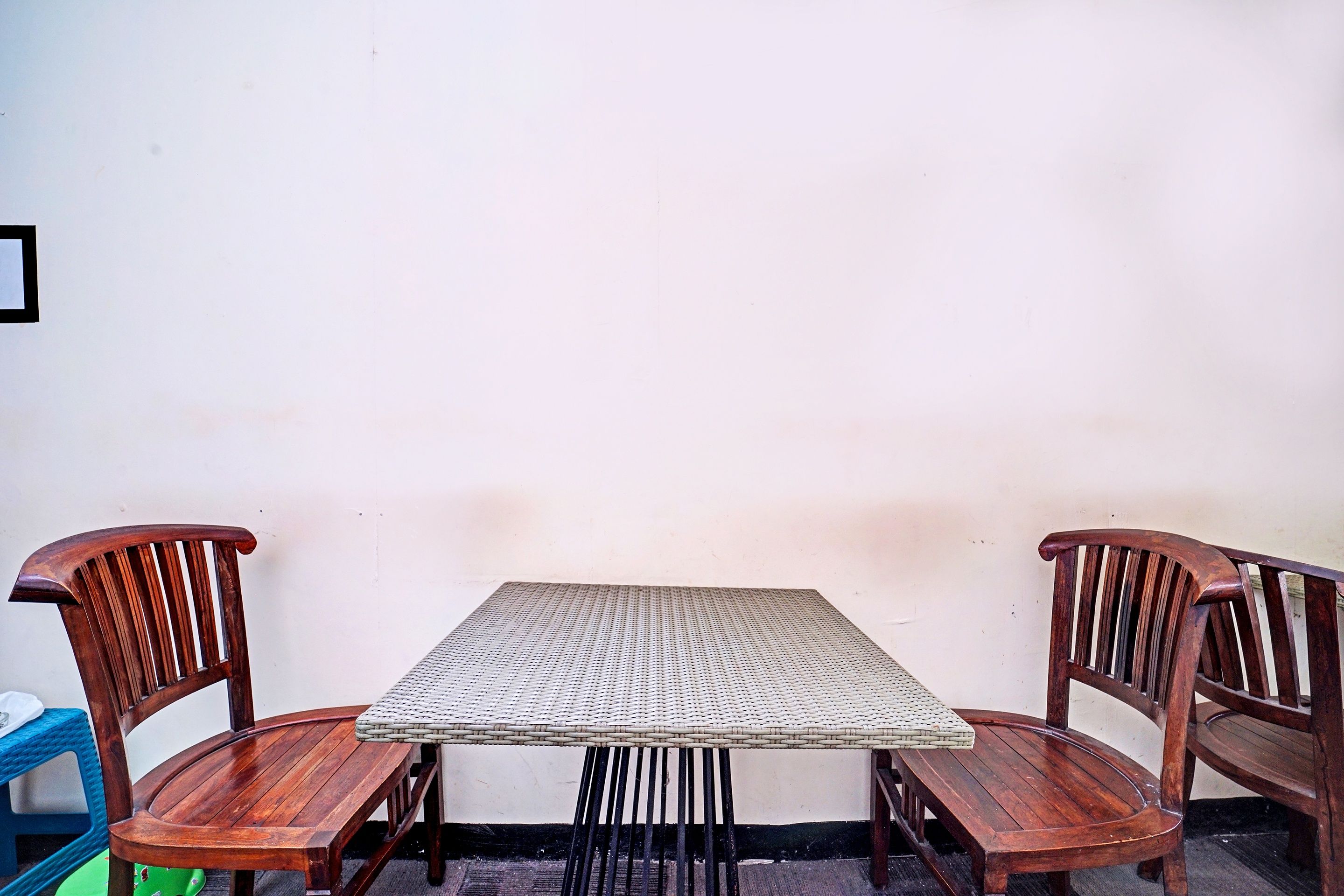 A square table with a woven top, flanked by two wooden chairs with curved backs.