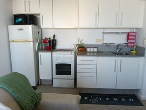 A compact kitchen with white cabinets, a refrigerator, a stove, and a microwave.
