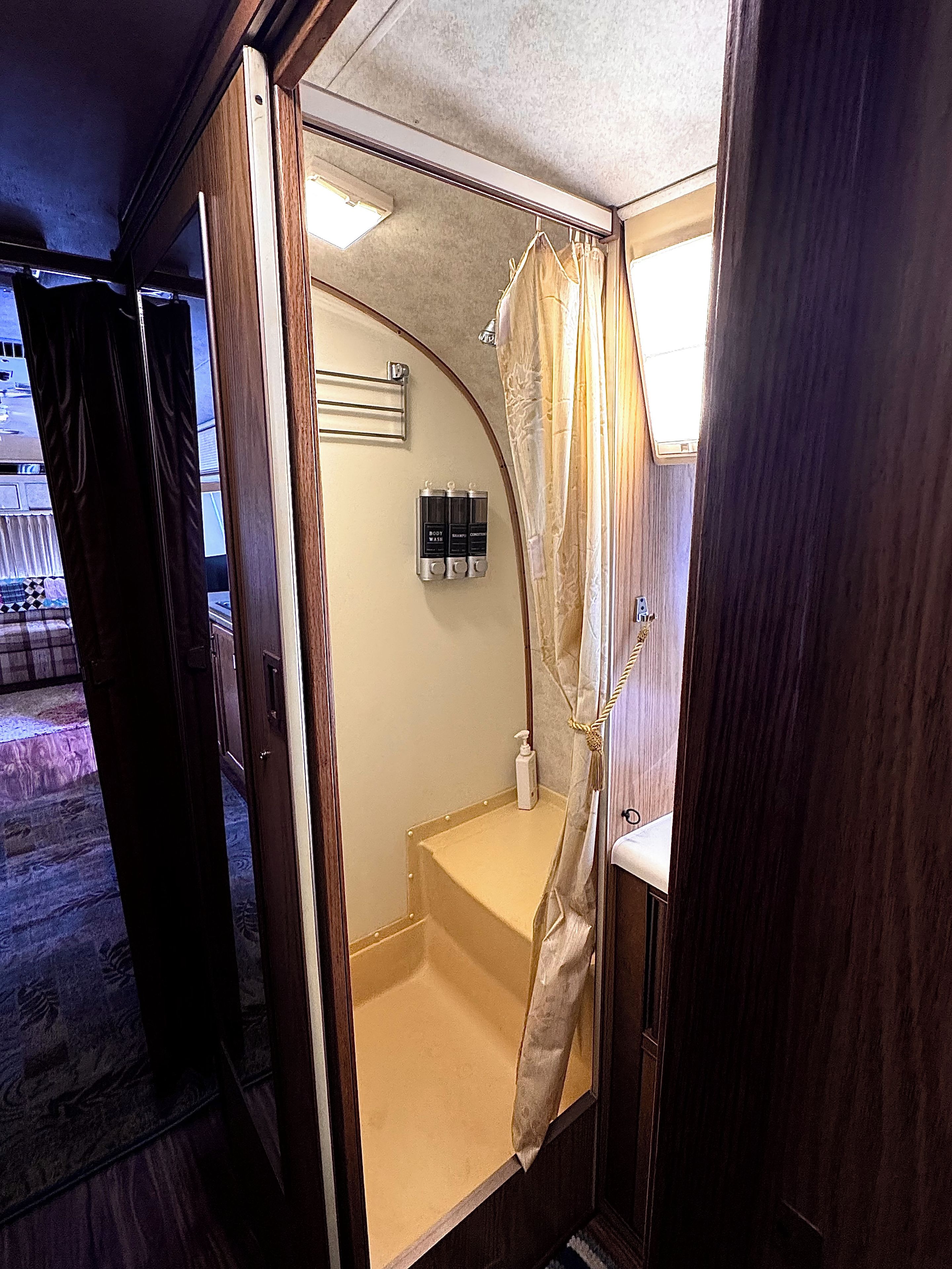 A compact bathroom with a shower, a towel rack, and a soap dispenser.