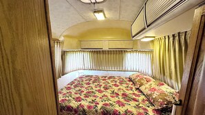Quarto compacto com cama, cortinas e aparelho de ar condicionado.