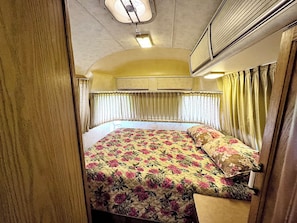Een kleine slaapkamer met een bed, gordijnen en een airconditioning.