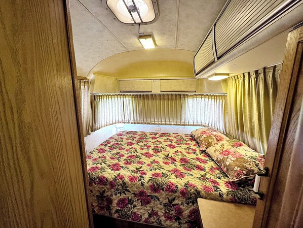 A compact bedroom with a bed, curtains, and an air conditioning unit.
