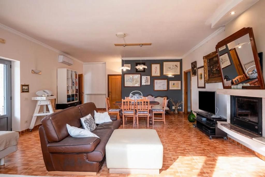 Una sala de estar con un sofá marrón, una mesa de comedor con sillas, una chimenea y un televisor.