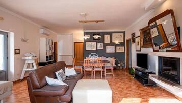 Una sala de estar con un sofá marrón, una mesa de comedor con sillas, una chimenea y un televisor.