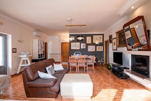 A living room with a brown sofa, a dining table with chairs, a fireplace, and a television. - Oasidipacefasano  (Fasano)