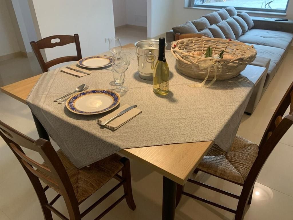 Une table à manger est dressée avec des assiettes, des couverts, des verres et une bouteille de vin, et un panier de pain est posé sur la table.