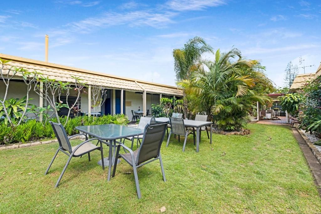 An outdoor seating area with tables and chairs, surrounded by greenery and a building with a tiled roof.