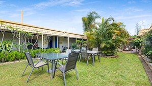 An outdoor seating area with tables and chairs, surrounded by a well-maintained lawn and tropical plants. - Coral Villa Motel (Svensson Heights)