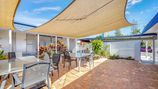 An outdoor patio area with a table and chairs, a pool office sign, and a covered seating area. - Coral Villa Motel (Svensson Heights)