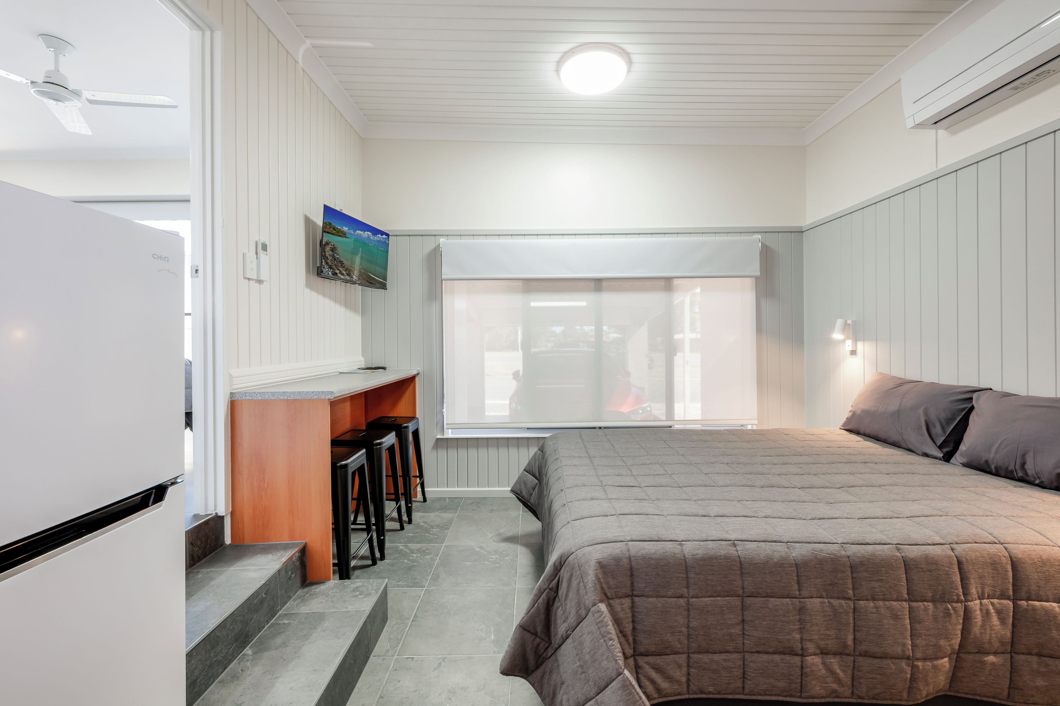 A bedroom with a bed, a desk, and a chair. There is a window with a view of the outside.