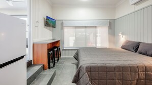 A bedroom with a bed, a desk, and a chair. There is a window with a view of the outside. - Coral Villa Motel (Svensson Heights)