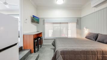 A bedroom with a bed, a desk, and a chair. There is a window with a view of the outside.