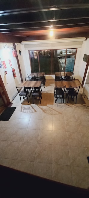 Un comedor con una mesa grande y sillas, un extintor en la pared, y vistas a través de la ventana.