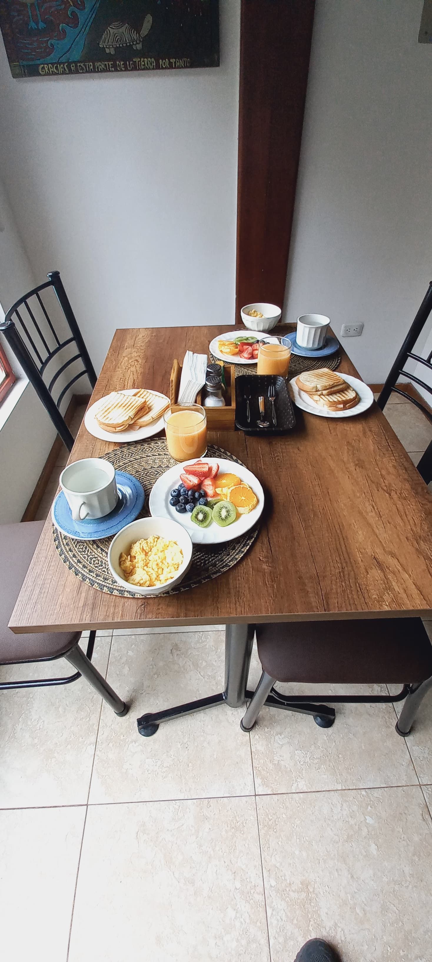 Una mesa de comedor con alimentos para el desayuno, incluyendo tostadas, fruta y huevos revueltos.