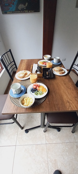 Une table à manger avec des aliments pour le petit-déjeuner, notamment des toasts, des fruits et des œufs brouillés.