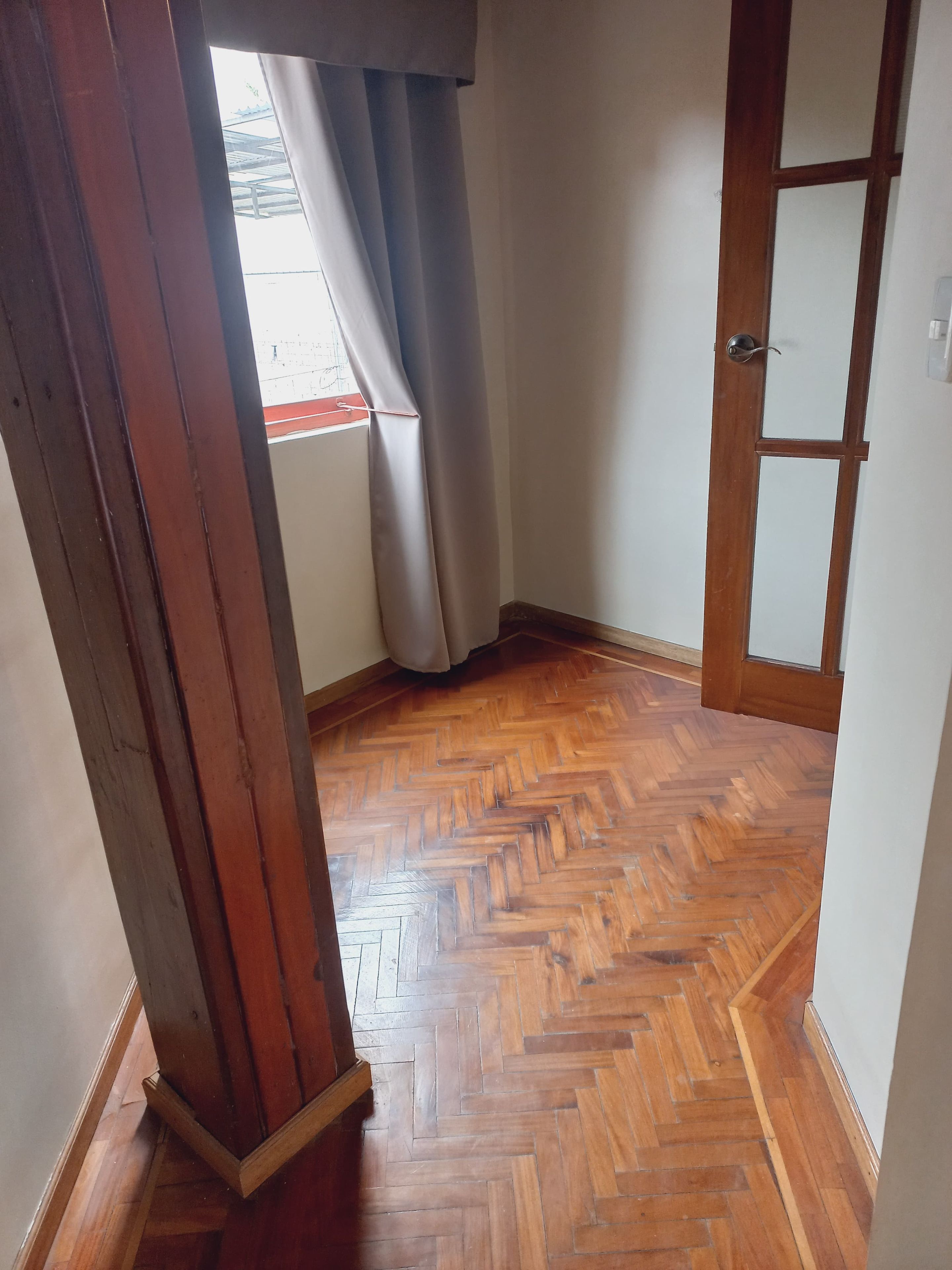 A hallway with a wooden herringbone floor, a wooden door, and a window with curtains.