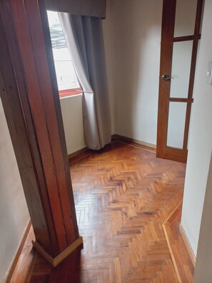 Un couloir doté d’un parquet en bois disposé en chevrons, d’une porte en bois et d’une fenêtre avec des rideaux.