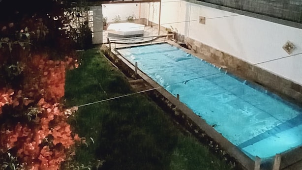 A swimming pool at night with a small hot tub and a white building in the background.