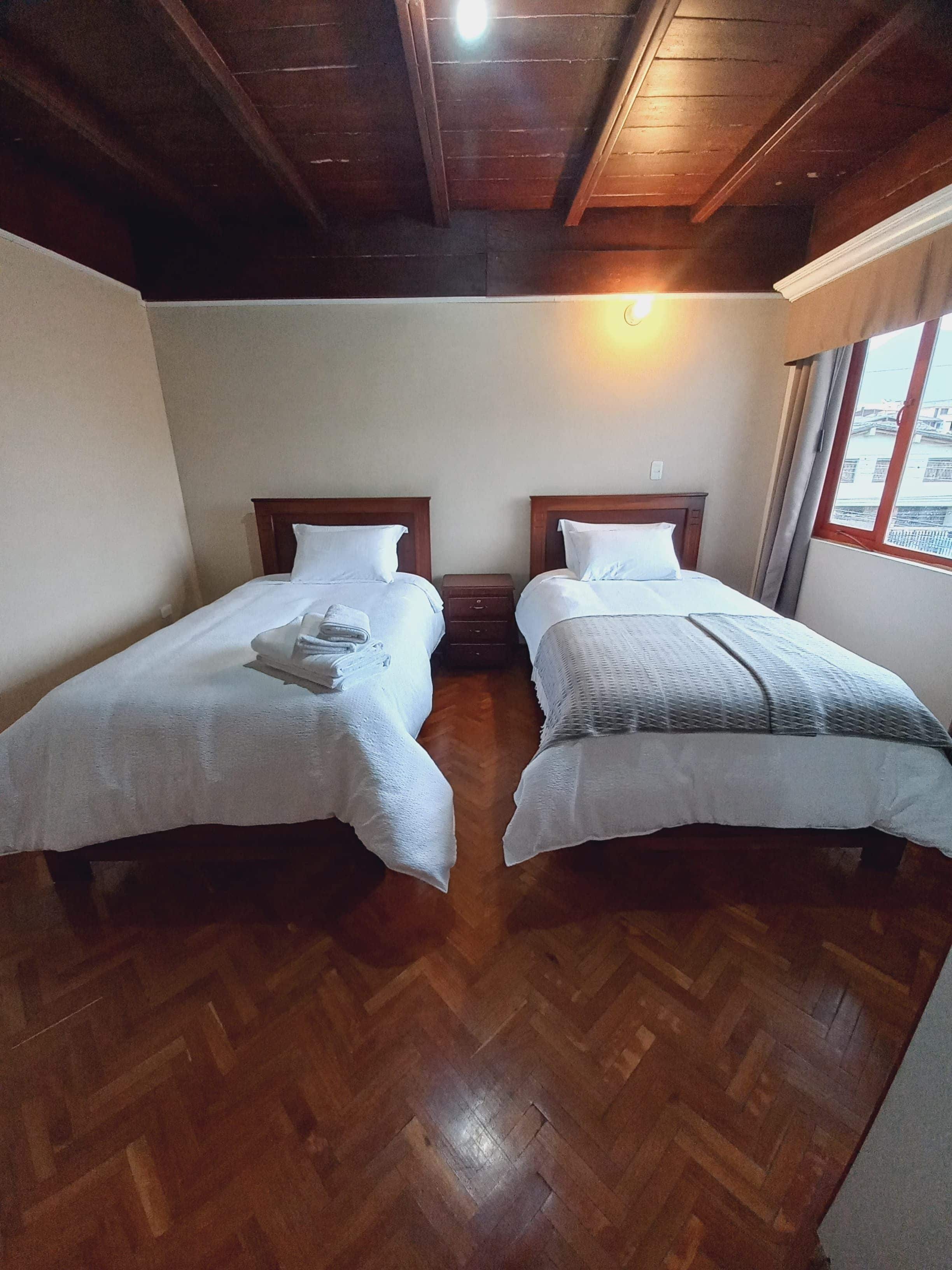 Habitación con dos camas, piso de madera y ventana con cortinas.