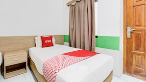 A hotel room with a bed, a nightstand, a wooden door, and a window with curtains. - Hotel O Mamagayo Inn (Yogyakarta)