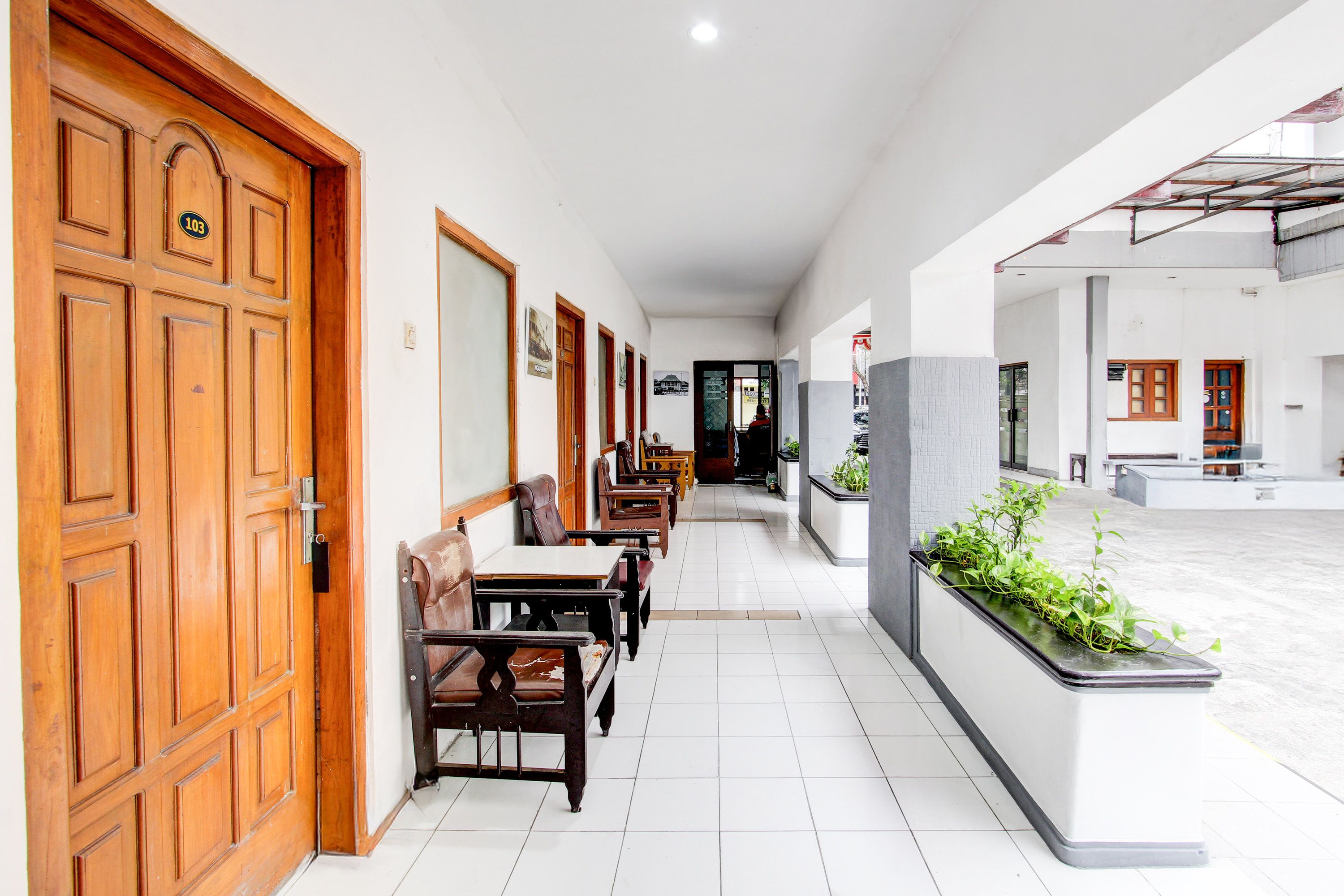 A corridor with wooden doors, seating area with tables and chairs, and a view of the street.