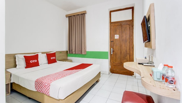 A hotel room with a bed, a wooden door, a small table with a TV, and a window with curtains. - Hotel O Mamagayo Inn (Yogyakarta)