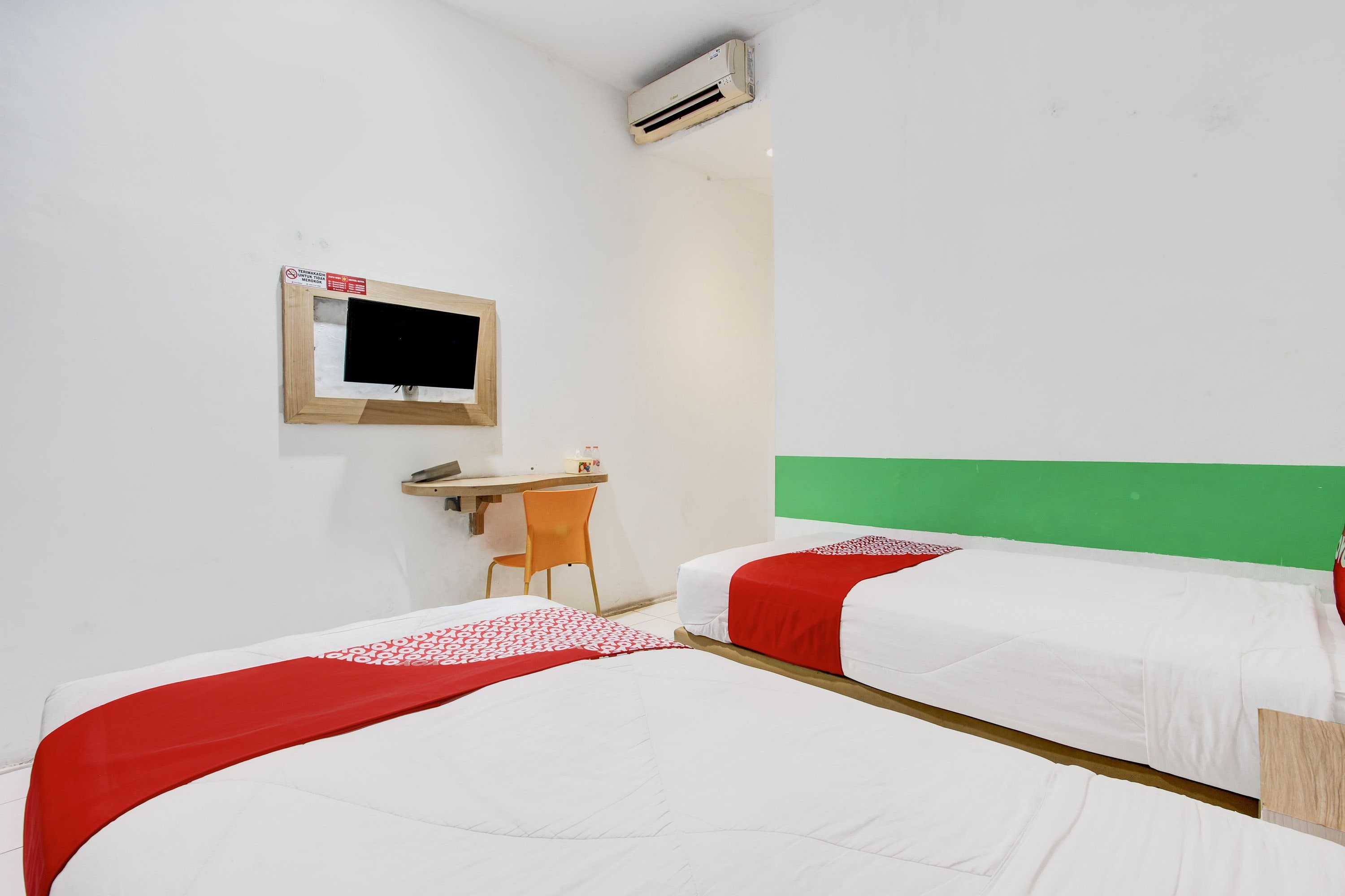 Una habitación de hotel con dos camas, un escritorio, una silla y un televisor instalado en la pared.