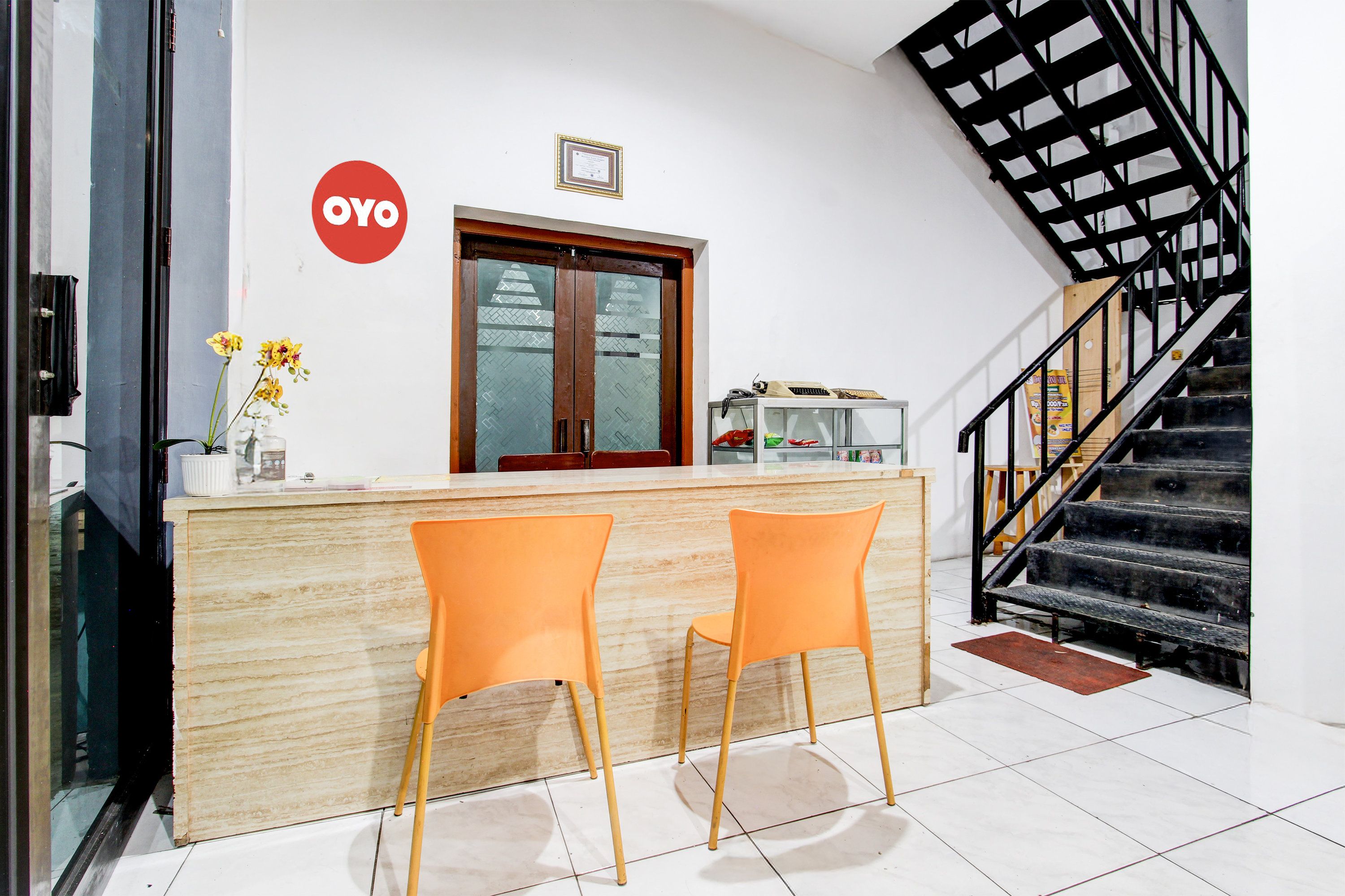 Un área de recepción con un mostrador de madera, dos sillas naranjas, una escalera y un cartel en la pared.