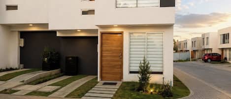 A modern two-story residential building with a flat roof, a front garage, and a well-maintained lawn.