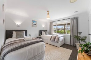 A hotel room with two beds, a large window with curtains, a bedside table, and a plant. - Cosy Corner on Macdonell (Taupo)
