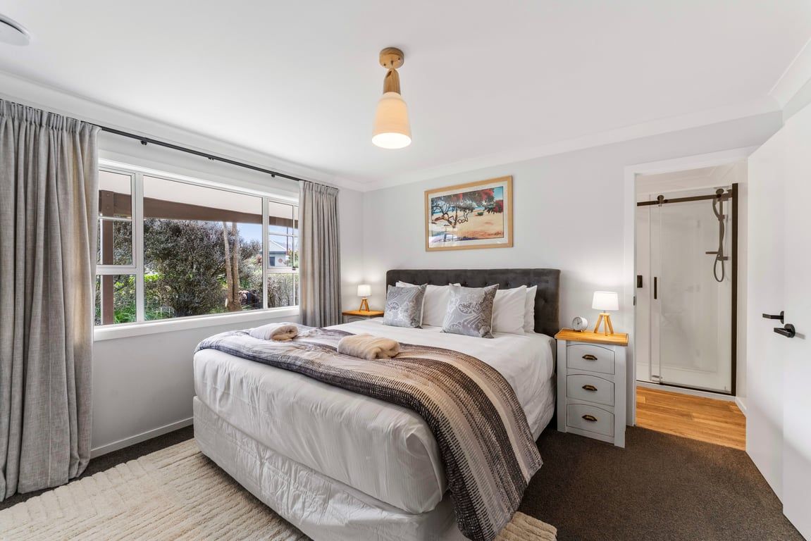 A bedroom with a large bed, bedside tables, a wardrobe, a window with curtains, and a painting on the wall.