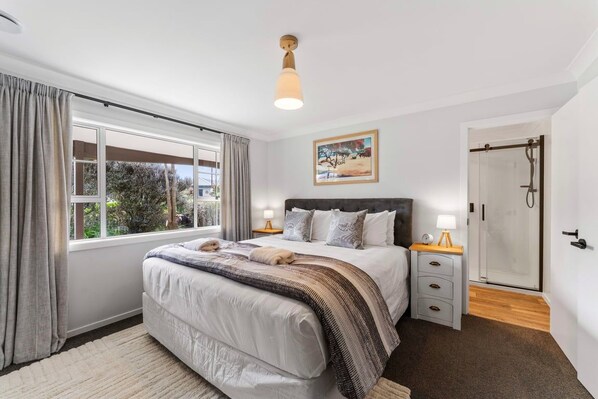 Une chambre à coucher avec un grand lit, des tables de chevet, une armoire, une fenêtre avec des rideaux et un tableau au mur.