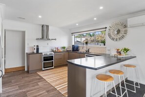 A modern kitchen with a central island, bar stools, a built-in oven, and a decorative wall clock. - Cosy Corner on Macdonell (Taupo)