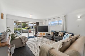 Un salon moderne avec un canapé, un fauteuil et un téléviseur à écran plat. Une grande fenêtre offre une vue sur l’extérieur.